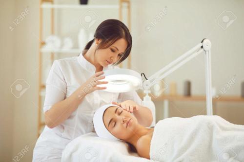 155130363-curing-skin-problems-cropped-female-cosmetologist-looking-at-clients-face-through-magnifying-lamp-ex