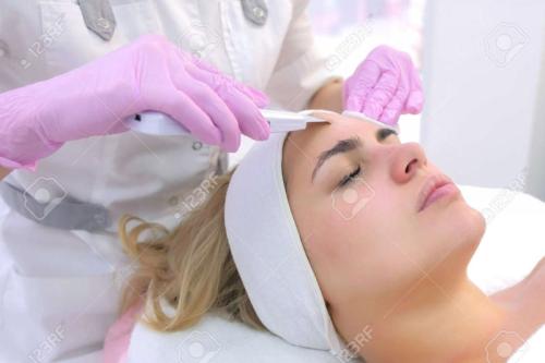 167950315-cosmetologist-making-ultrasonic-face-cleaning-procedure-for-young-woman-in-clinic-closeup-client-por